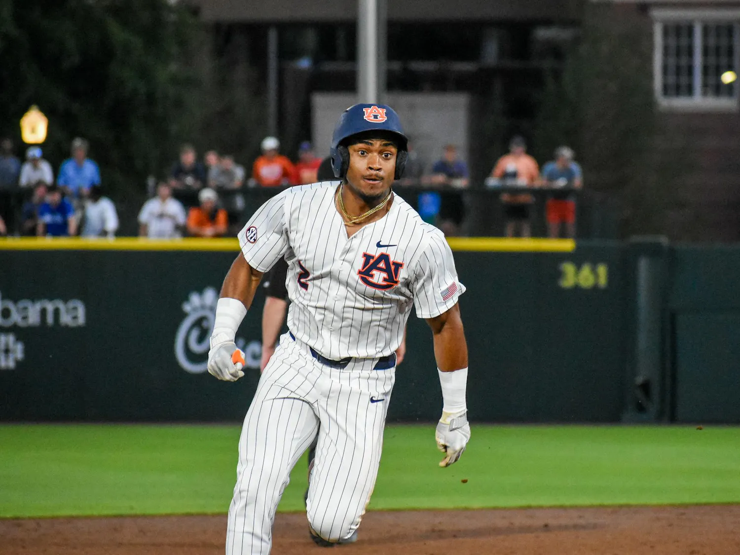 A baseball player in a striped uniform runs on the field, with spectators visible in the background.
