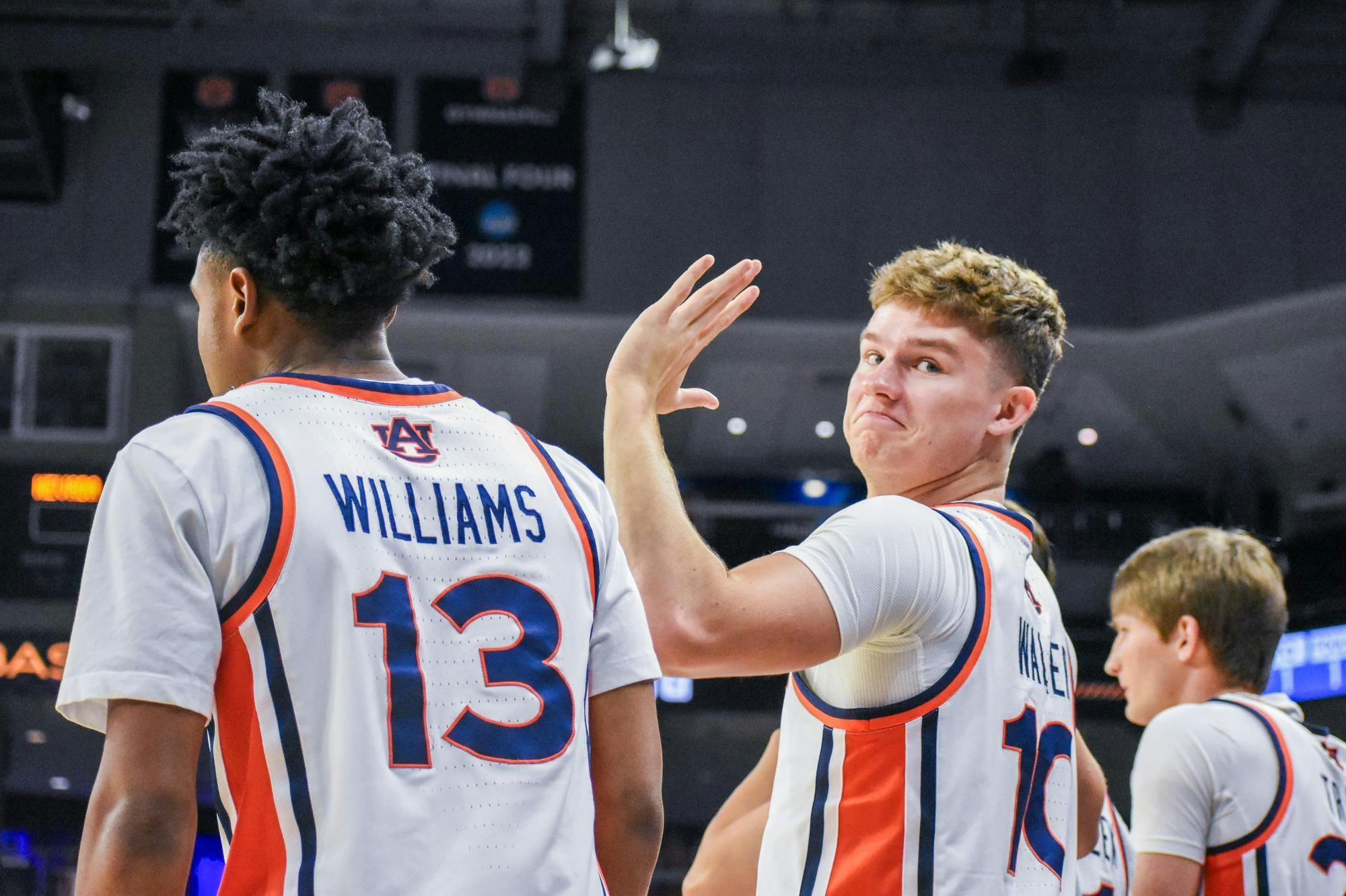 Two basketball players in jerseys with "WILLIAMS" and "MATEER" on the back are in a gym, with one player smiling and waving.