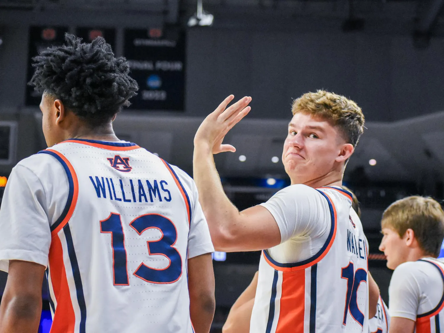 Two basketball players in jerseys with "WILLIAMS" and "MATEER" on the back are in a gym, with one player smiling and waving.