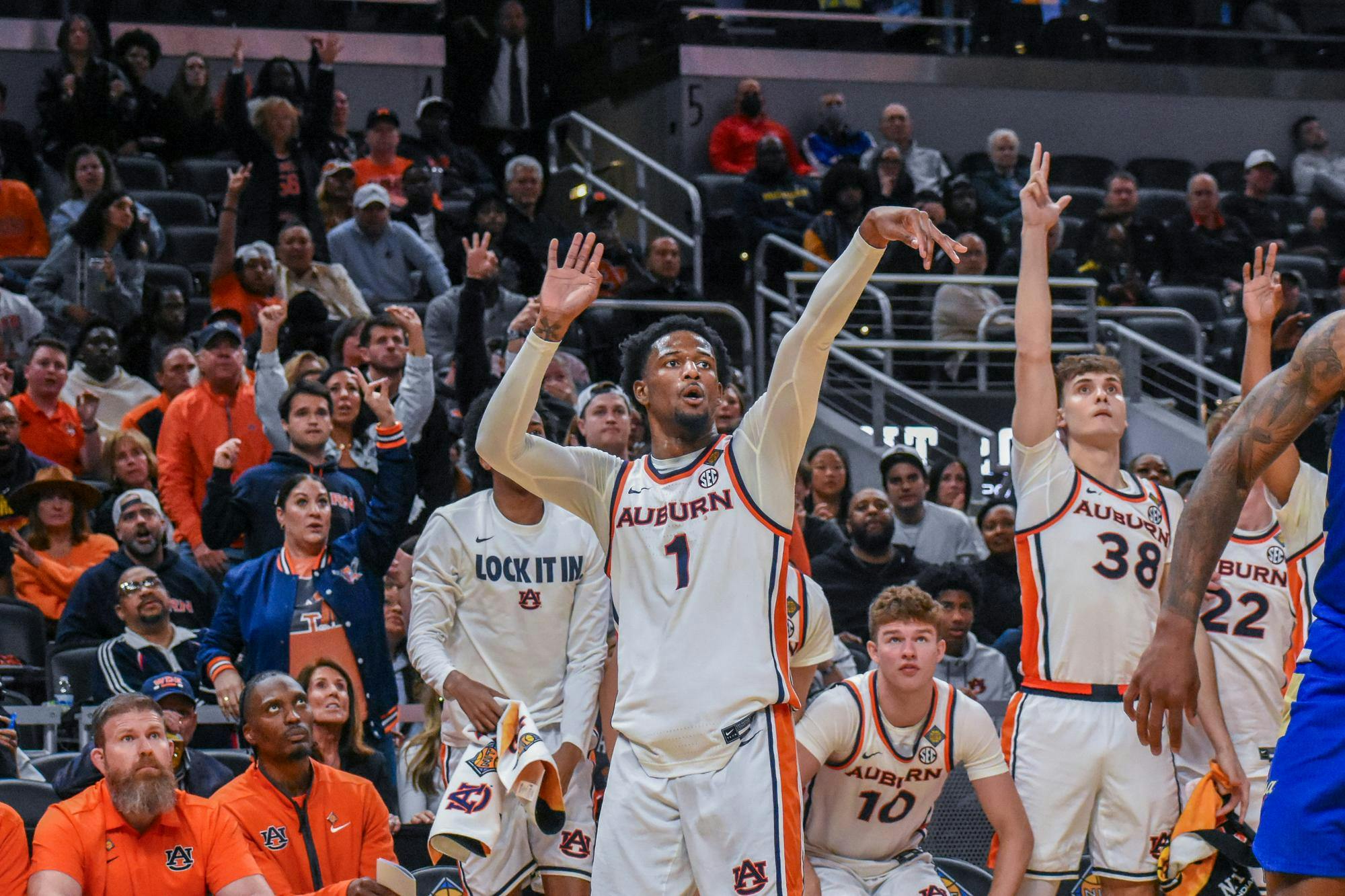 A basketball player in an Auburn uniform is shooting, while teammates and an enthusiastic crowd cheer from the sidelines.
