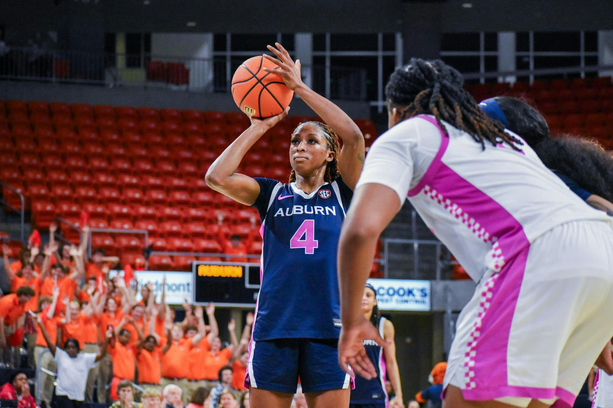A player in a blue basketball jersey is preparing to shoot while spectators in orange shirts cheer in the background.