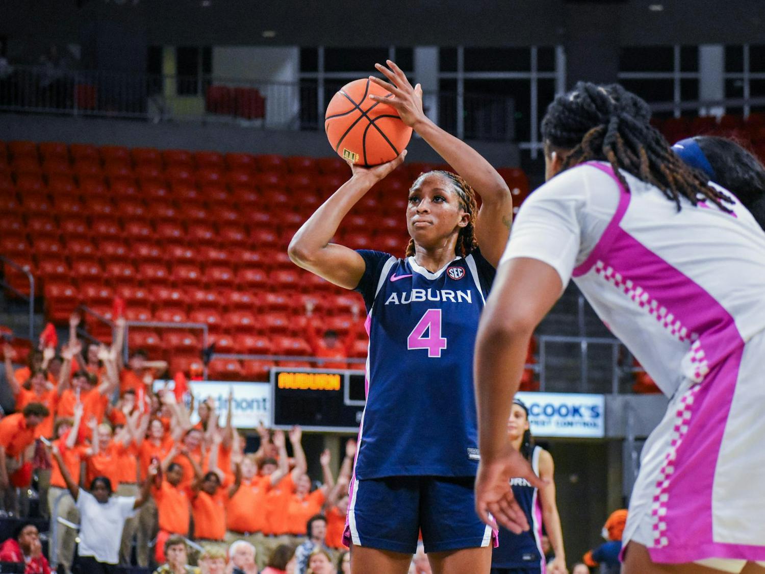 A player in a blue basketball jersey is preparing to shoot while spectators in orange shirts cheer in the background.