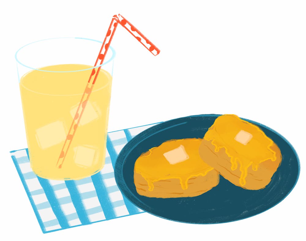 There is a dark blue plate holding two sweet potato biscuits covered in honey and butter while a cup of lemonade and a light blue gingham napkin sit next to it. 