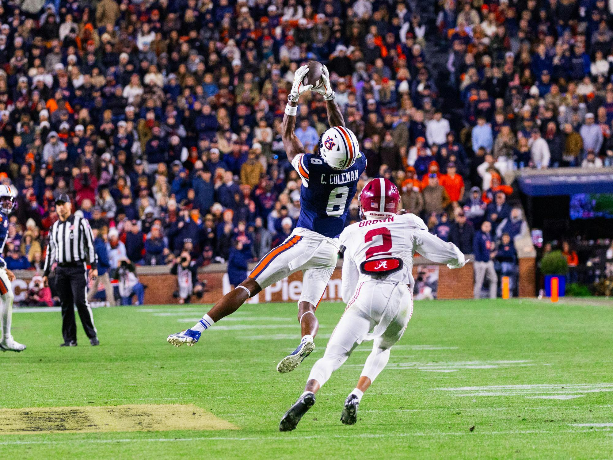 A football player in a blue uniform leaps to catch a pass while being pursued by a player in white.