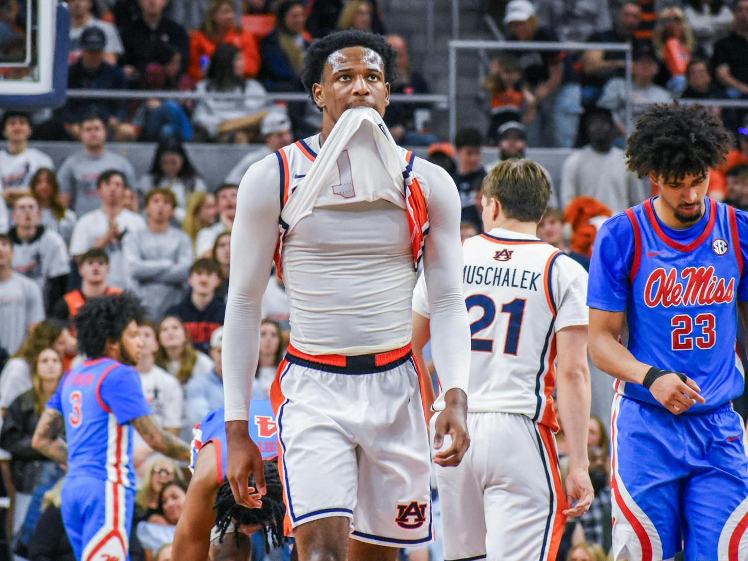 A basketball player in a white jersey pulls a shirt over his mouth while other players and a cheering crowd are in the background.