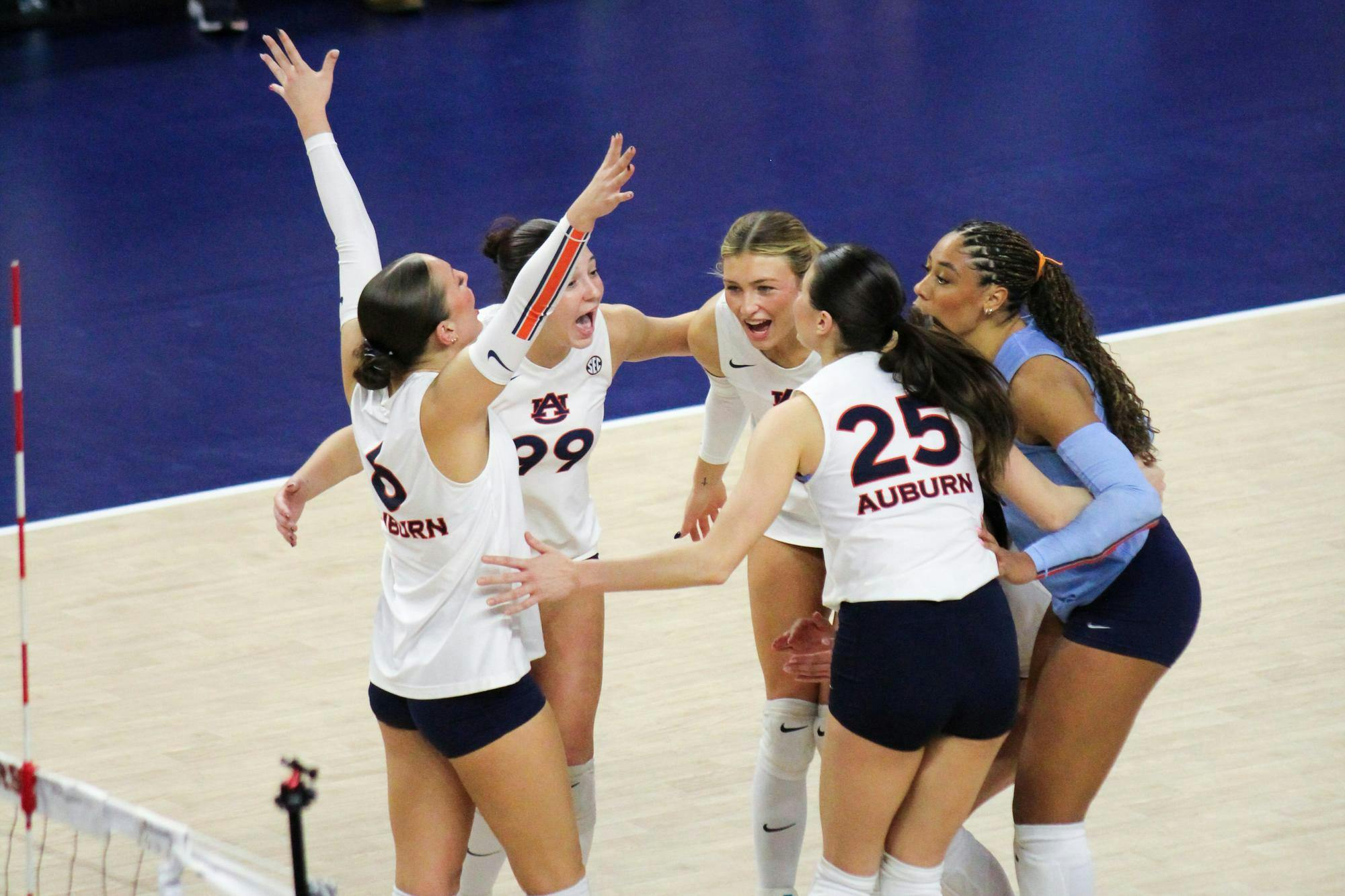 A group of five volleyball players, wearing matching uniforms, celebrate enthusiastically in a sports venue.
