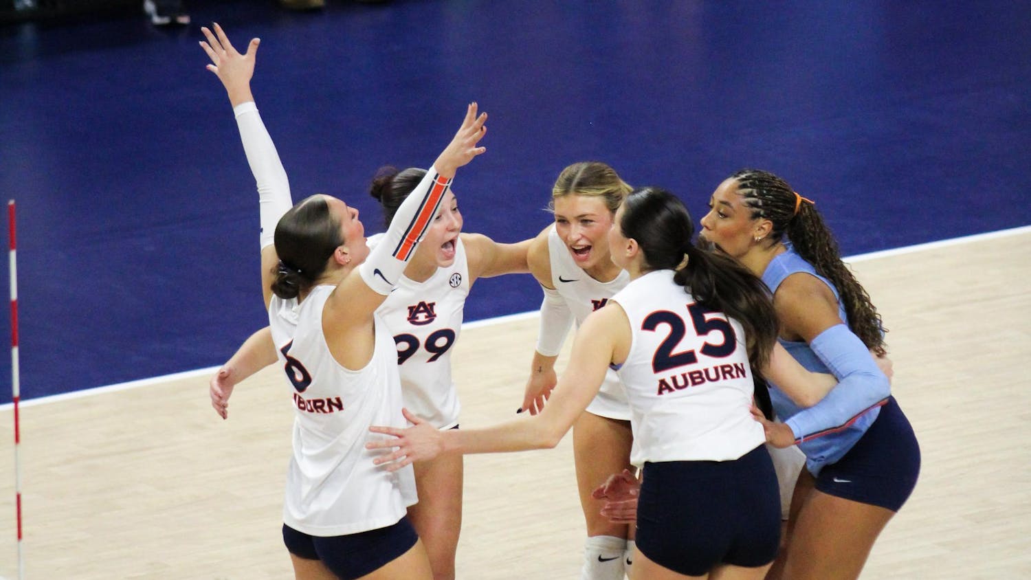 A group of five volleyball players, wearing matching uniforms, celebrate enthusiastically in a sports venue.