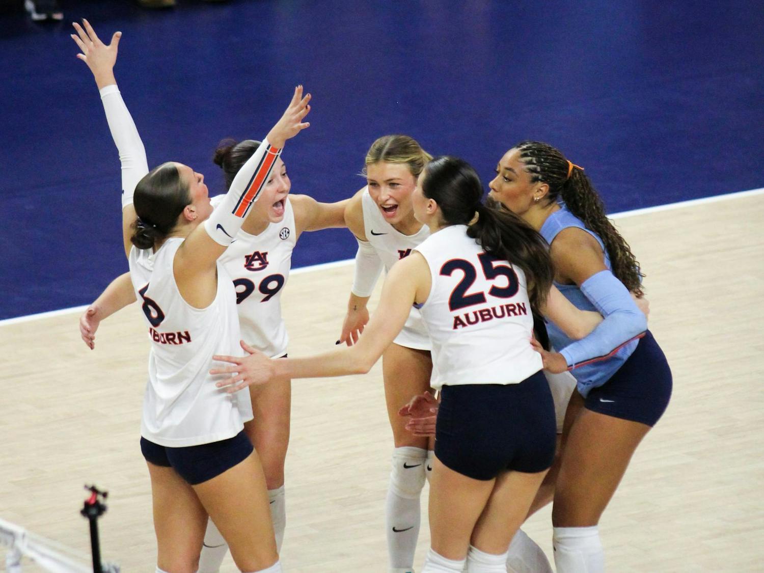 A group of five volleyball players, wearing matching uniforms, celebrate enthusiastically in a sports venue.