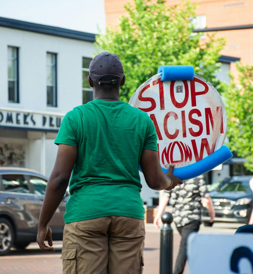 <p>&nbsp;Damarius Nolan-Watts, one of the original members of the sit-in, holds a sign saying "STOP RACISM NOW" on Toomer's Corner.</p>