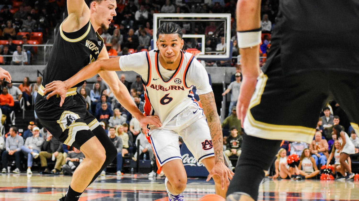 A player in an Auburn uniform lunges for a basketball while two opponents are positioned nearby on a basketball court.