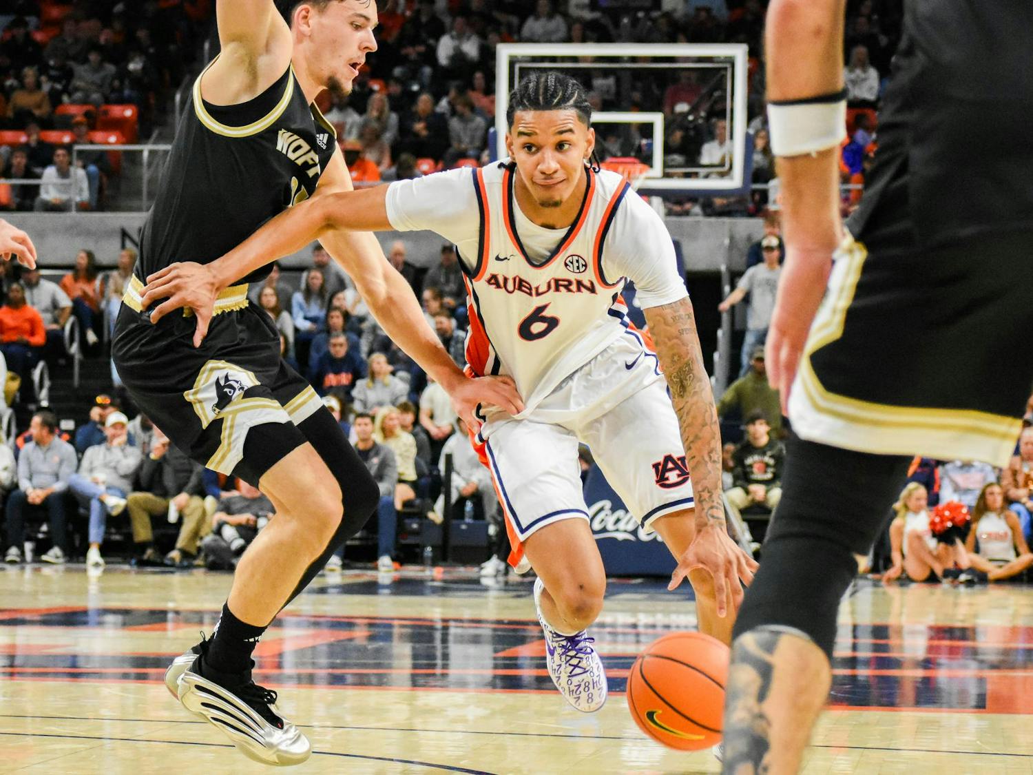 A player in an Auburn uniform lunges for a basketball while two opponents are positioned nearby on a basketball court.