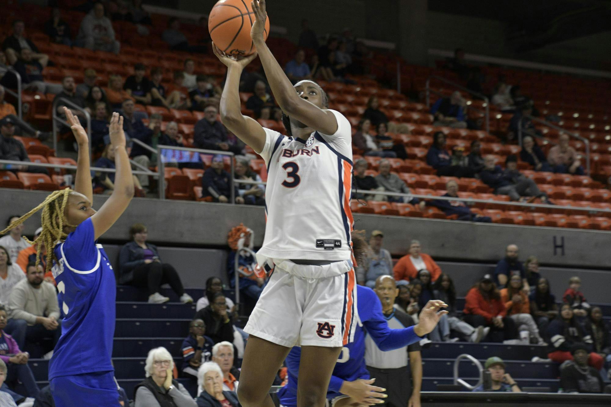 A basketball player in a white uniform jumps to shoot a ball while another player reaches to block.