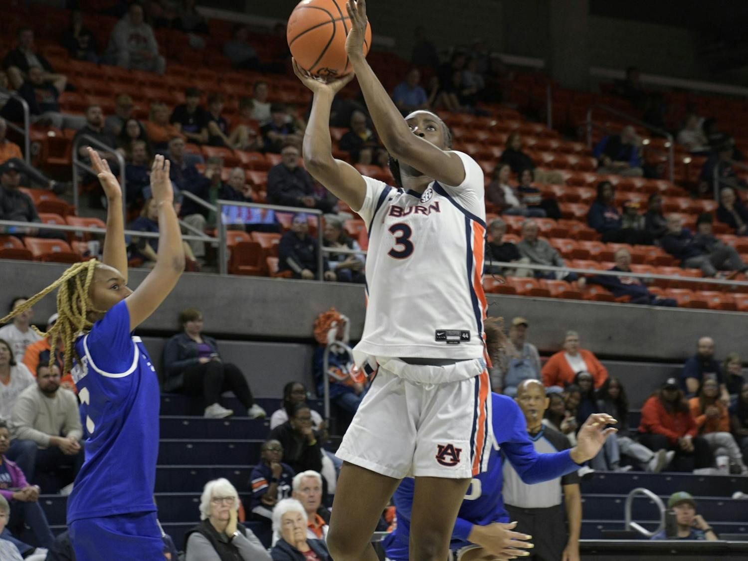 A basketball player in a white uniform jumps to shoot a ball while another player reaches to block.