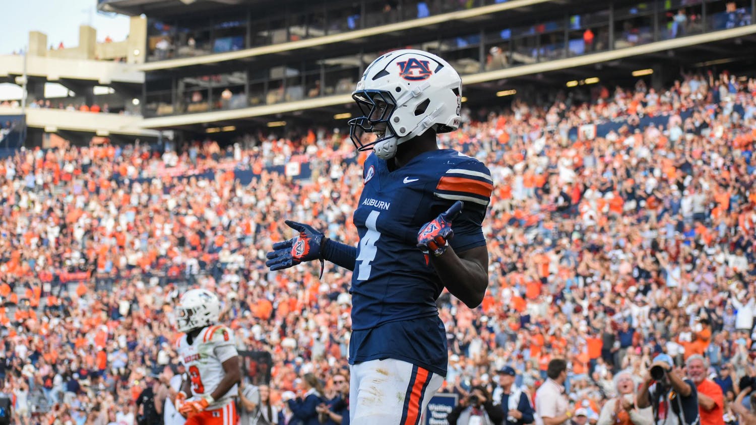 A football player in a blue and orange uniform celebrates as a cheering crowd fills the stadium behind him.