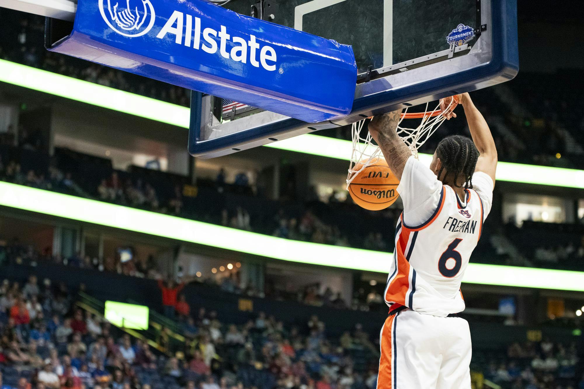 A basketball player hangs onto the hoop, holding a ball above a cheering crowd in a sports arena.