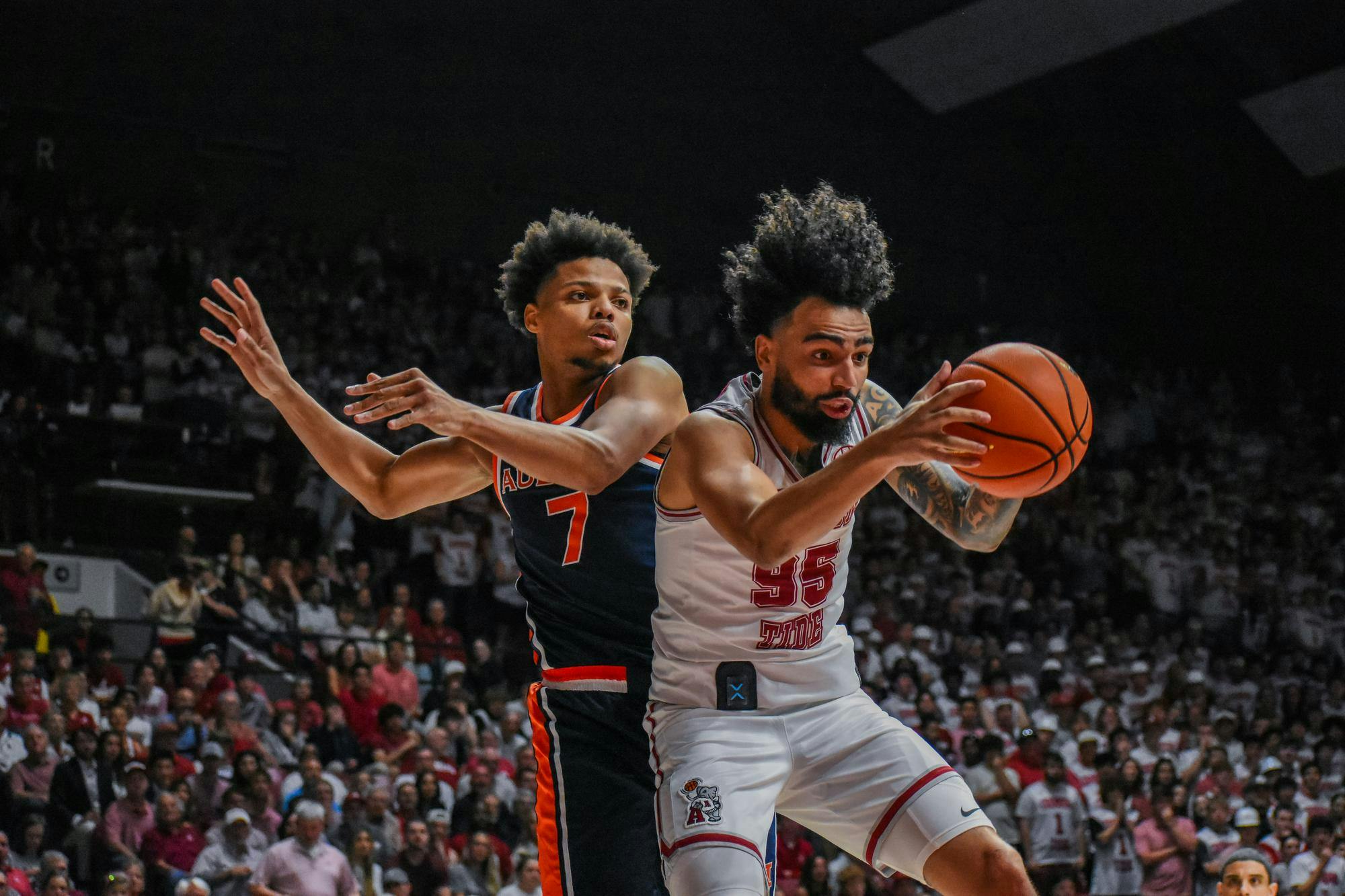 Two basketball players are in action, one attempting to seize the ball while the other reaches to block.