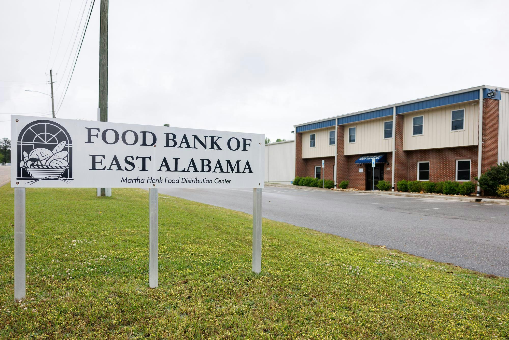 A large sign displays "FOOD BANK OF EAST ALABAMA" in bold letters, next to a modest brick building with multiple windows.