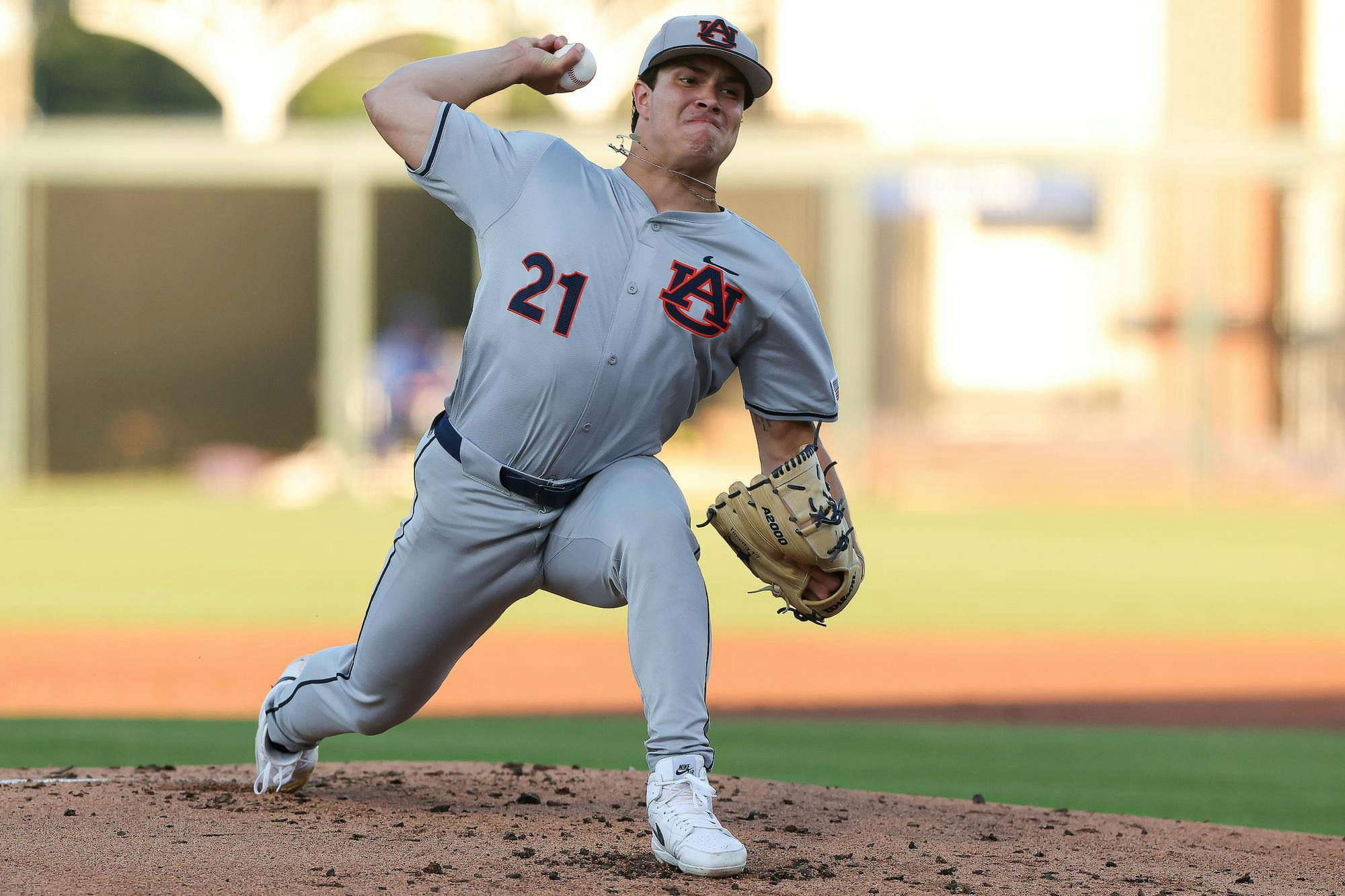 A player in a gray baseball uniform, wearing number 21, is pitching on a baseball mound with a focused expression.
