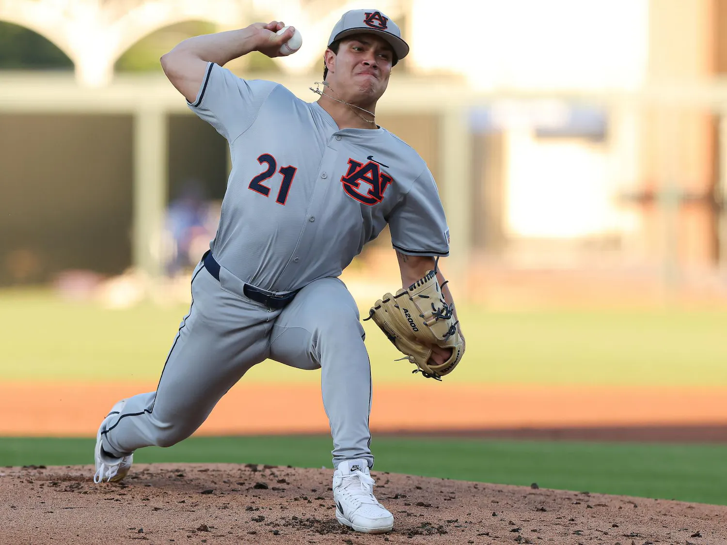 A player in a gray baseball uniform, wearing number 21, is pitching on a baseball mound with a focused expression.
