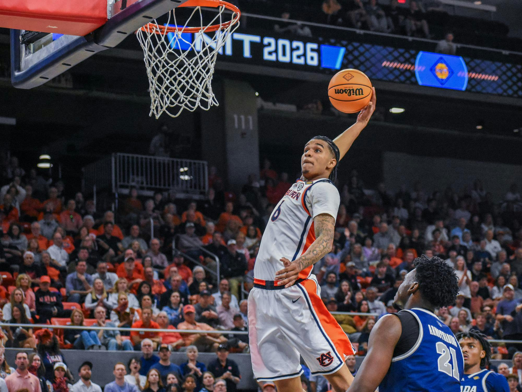 A player jumps to dunk a basketball while others watch in a crowded arena.