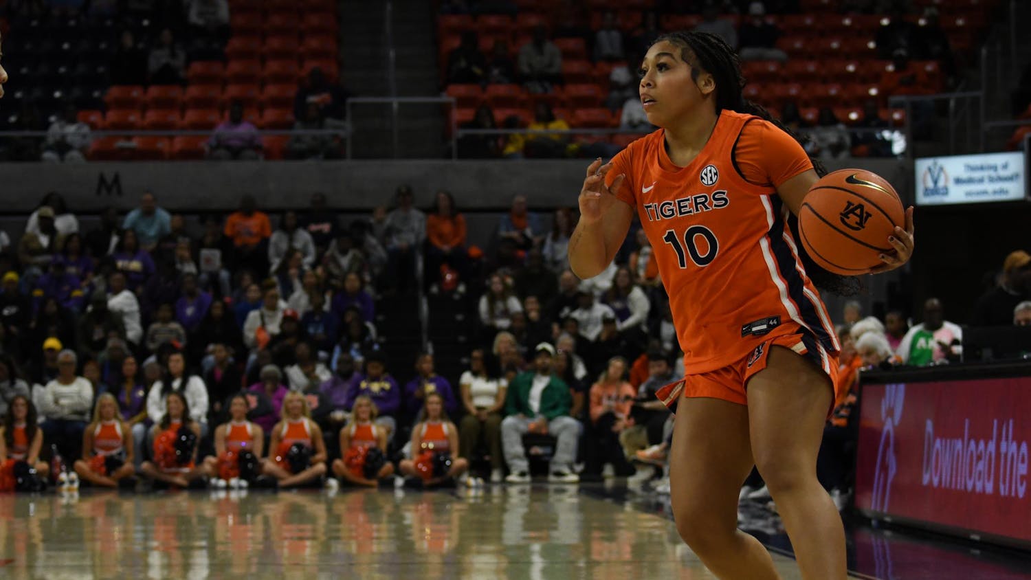 A female basketball player in an orange uniform dribbles a ball towards a crowd in a sports arena.