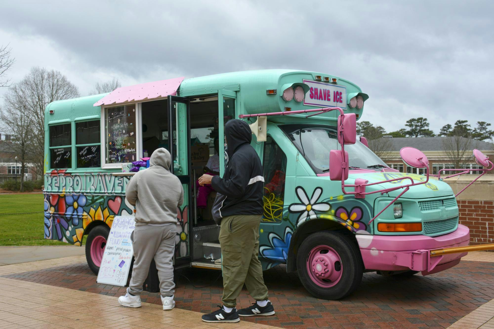 A brightly colored food truck with flowers painted on it is approached by two people in casual attire.