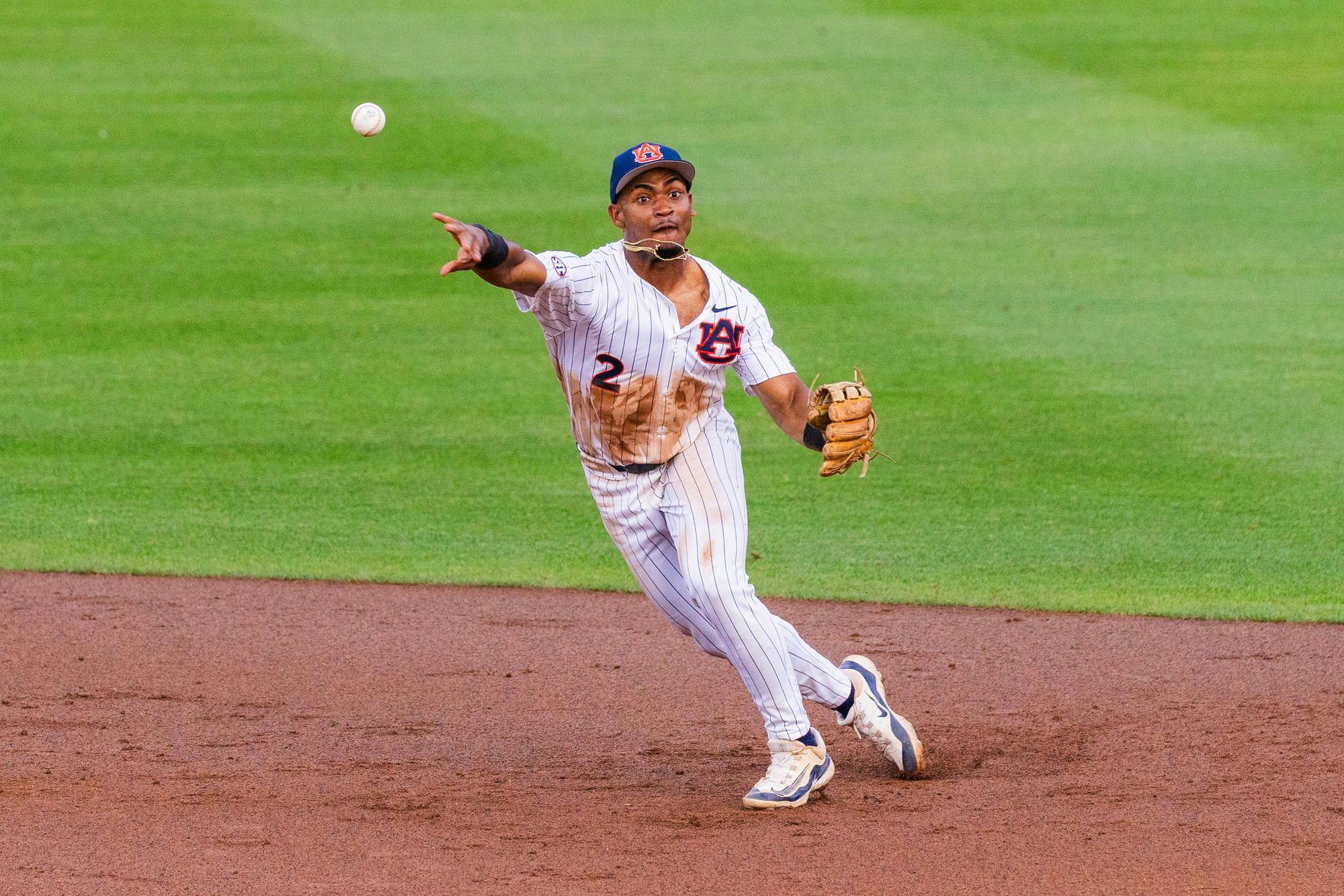 A player in a white and blue striped uniform is throwing a baseball while running on a dirt infield.
