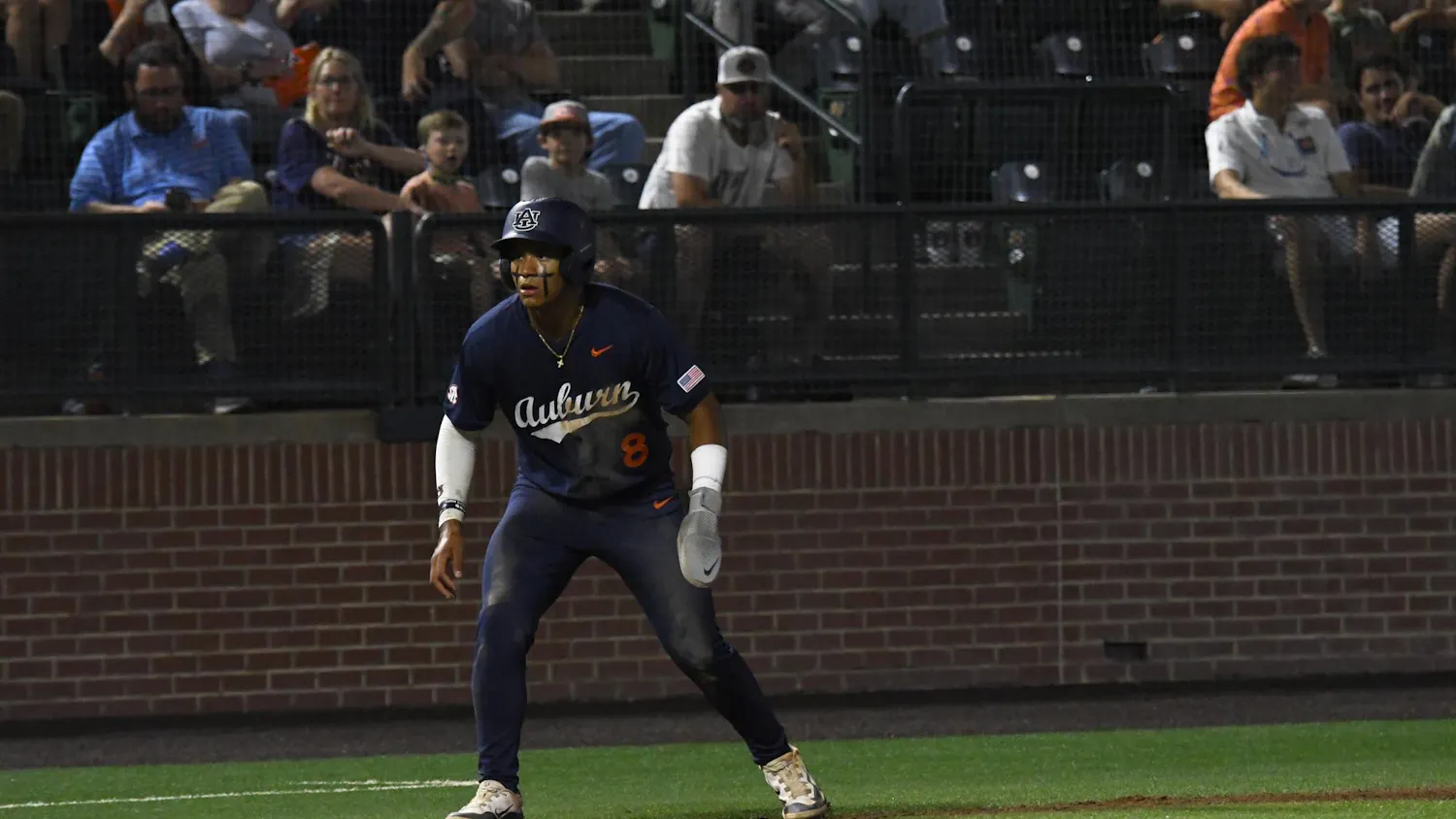 A baseball player in a dark jersey stands on a diamond, preparing to run, with spectators in the background.