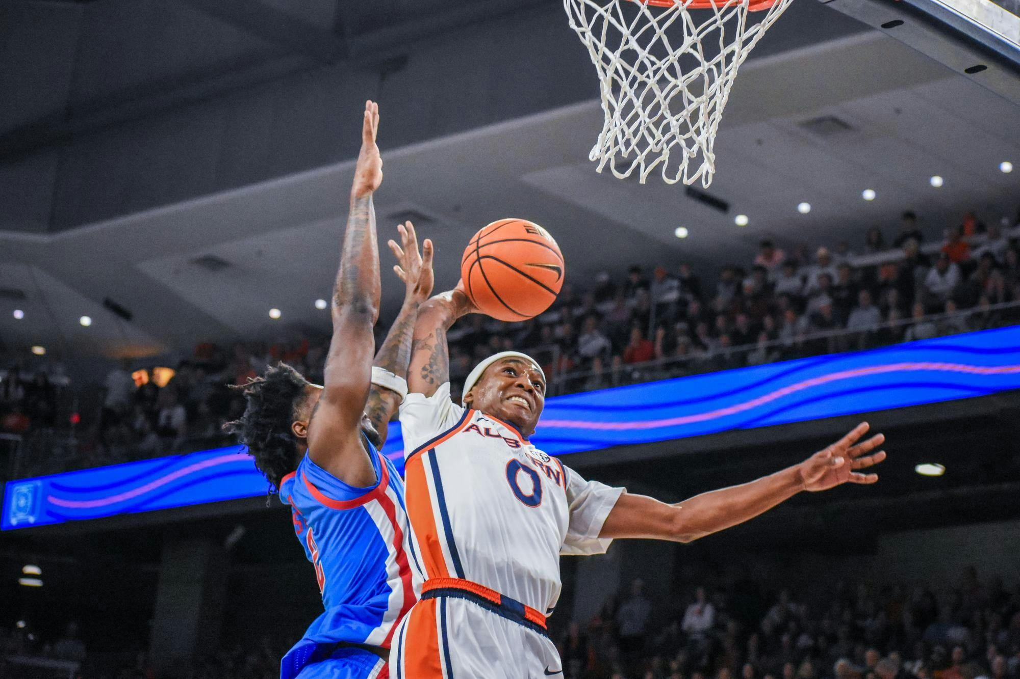 A player in a white and orange uniform leaps to score while another player in blue tries to block the shot.