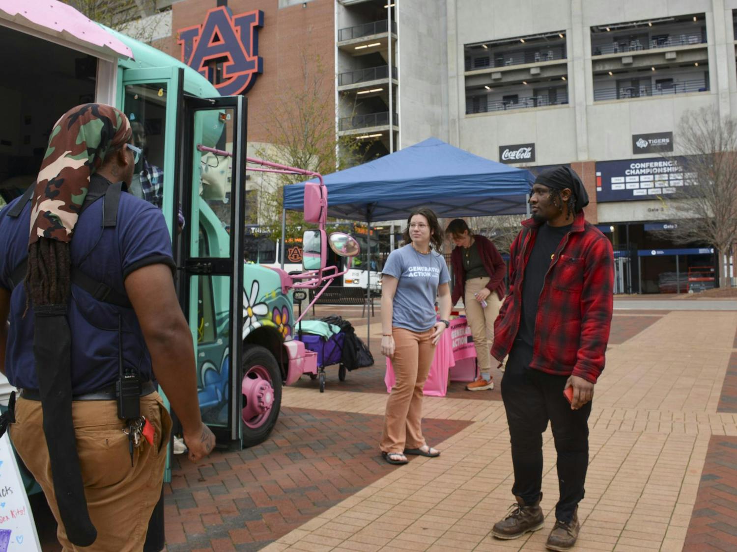 A colorful food truck is parked, with three people engaged in conversation nearby under a blue canopy.