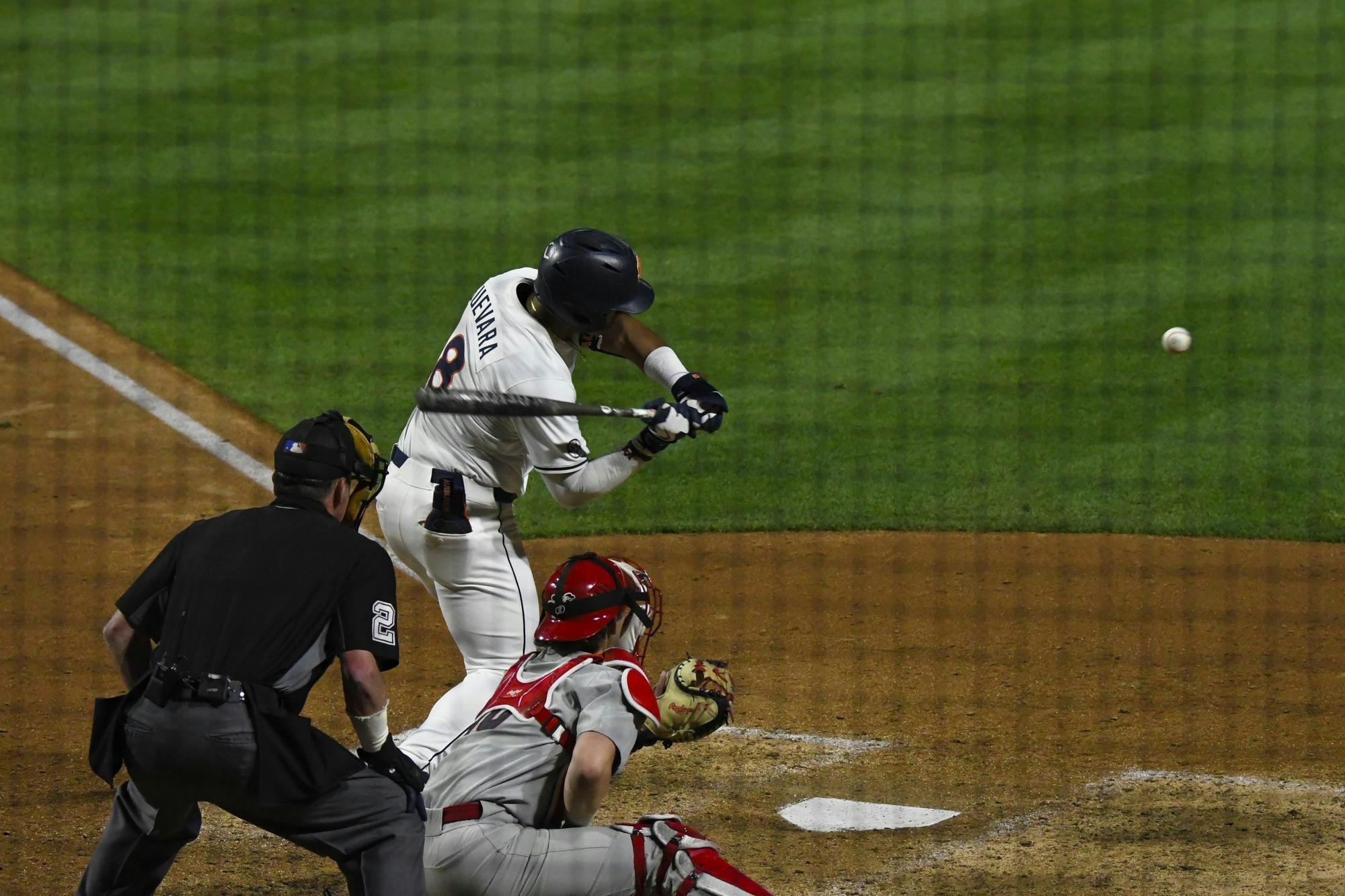A baseball player swings a bat at a ball while a catcher prepares to receive it, with an umpire observing.