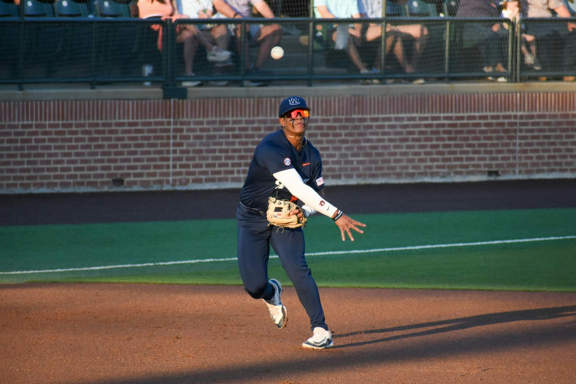 A baseball player in a dark uniform fields a ball, preparing to throw, with spectators in the background.