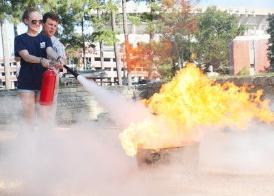 Savannah Renfroe, freahman in theater, practices using a fire extinguisher under the direction of Kenny Harrison, University fire safety manager. (Emily Adams/PHOTO EDITOR)