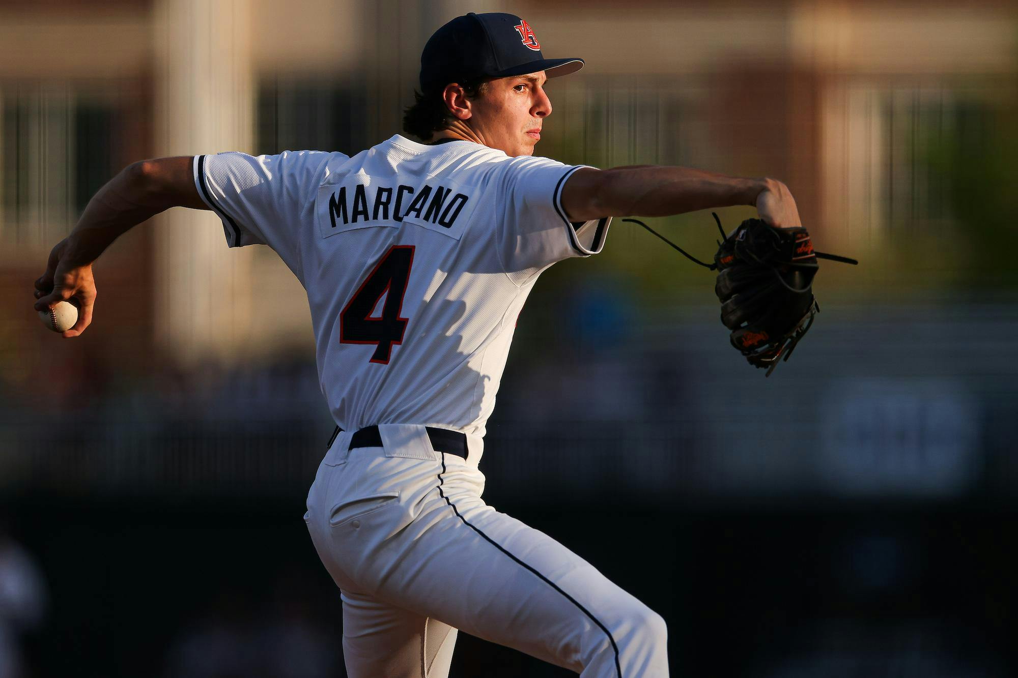 A baseball player in a white jersey with "MARCANO" and the number 4 prepares to pitch, holding a baseball in his gloved hand.