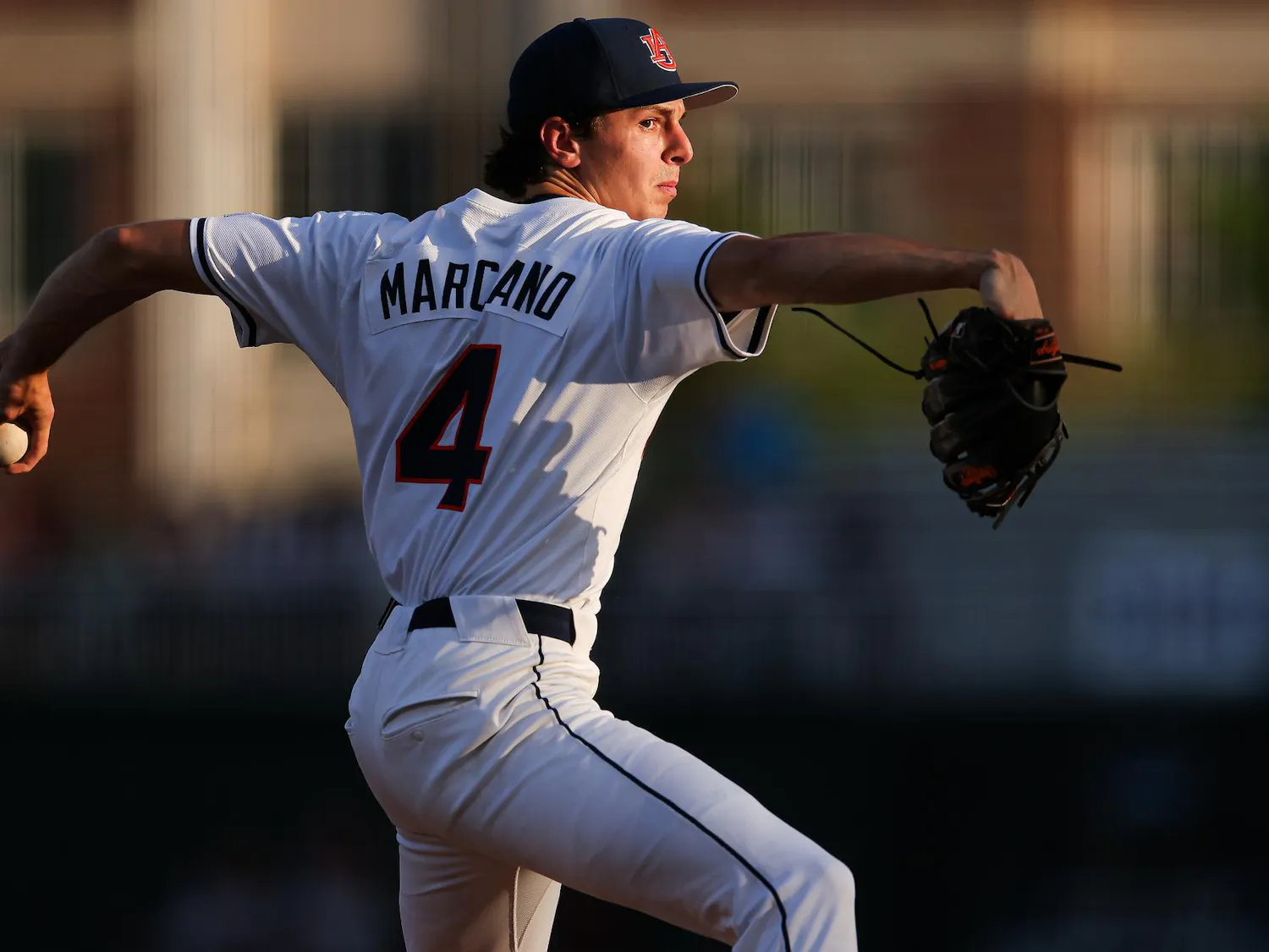 A baseball player in a white jersey with "MARCANO" and the number 4 prepares to pitch, holding a baseball in his gloved hand.