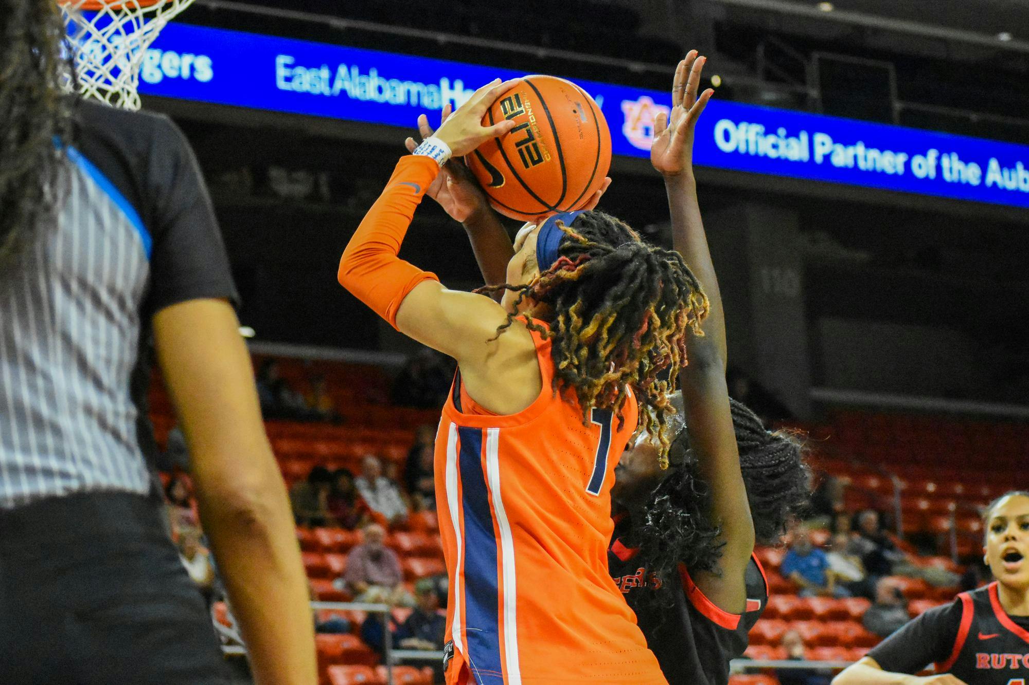 A player in an orange jersey jumps to score while being defended by an opponent in a black jersey near the basket.