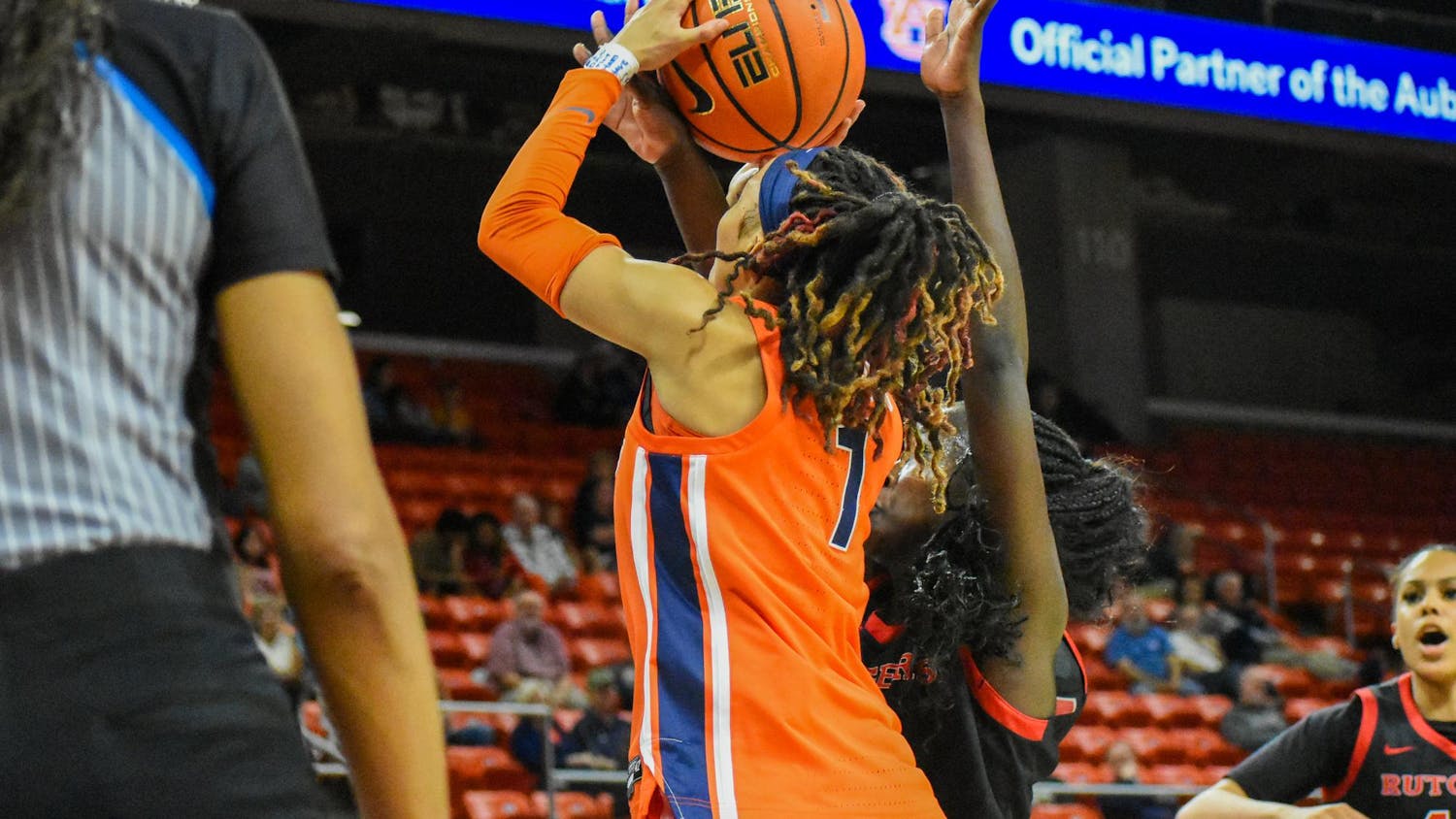A player in an orange jersey jumps to score while being defended by an opponent in a black jersey near the basket.