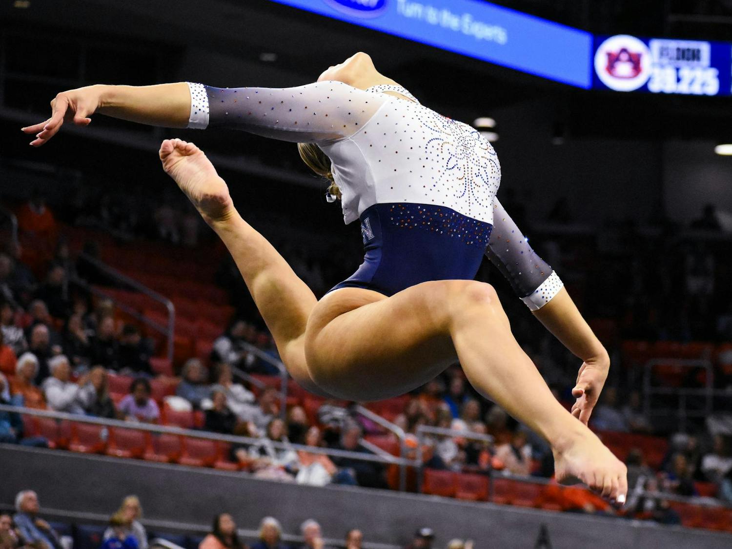 A gymnast performs an aerial leap, showcasing athleticism in a sparkly leotard above a crowd in a gymnasium.