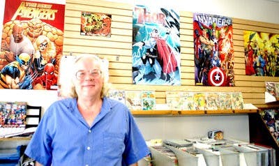 John Mullins, owner of Collector's Corner comic book store on E Glenn Avenue, stands in front of posters of his heroes. (Emily Clever / Copy Editor)