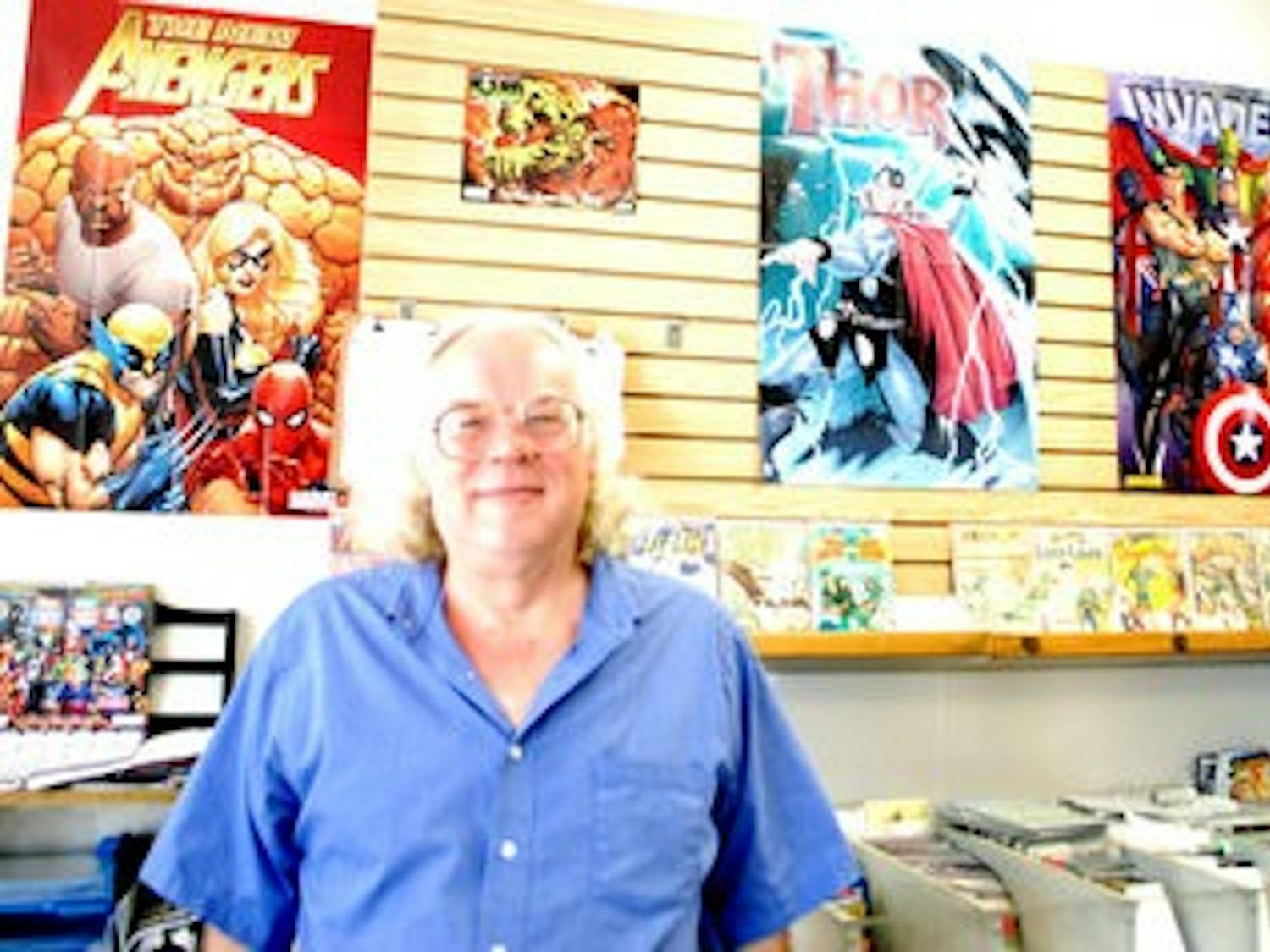 John Mullins, owner of Collector's Corner comic book store on E Glenn Avenue, stands in front of posters of his heroes. (Emily Clever / Copy Editor)