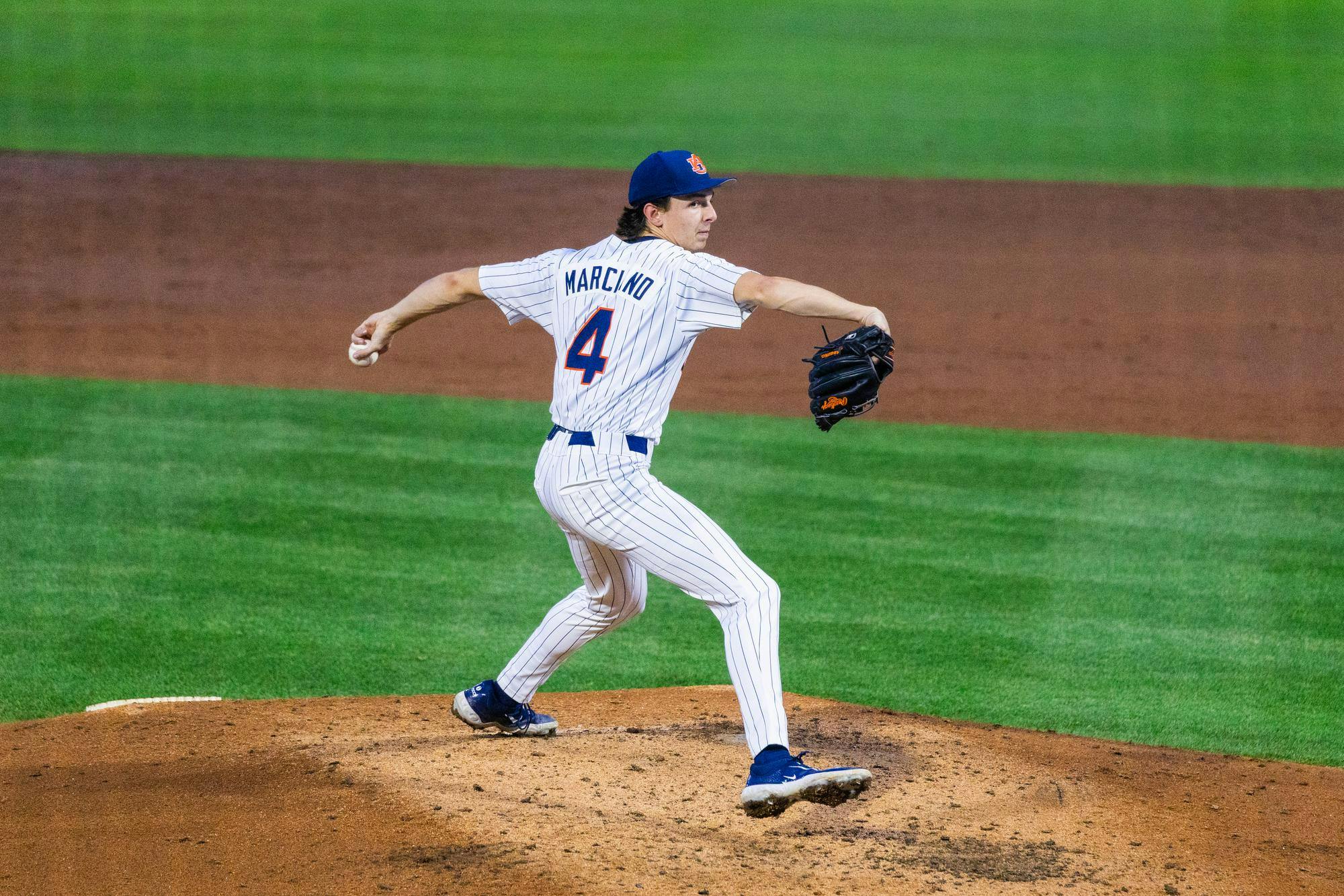 A baseball pitcher in a pinstriped uniform winds up to throw a pitch on a dirt mound.