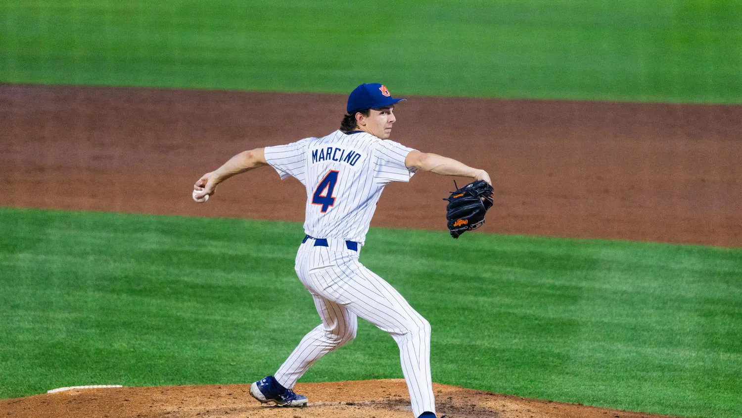 A baseball pitcher in a pinstriped uniform winds up to throw a pitch on a dirt mound.