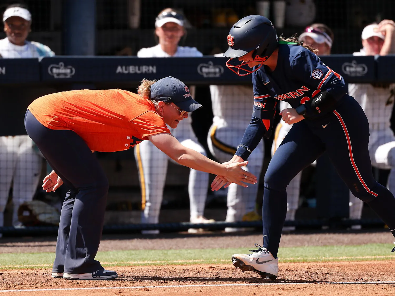 A coach in an orange shirt and cap extends her hand for a high five with a player in a blue uniform.