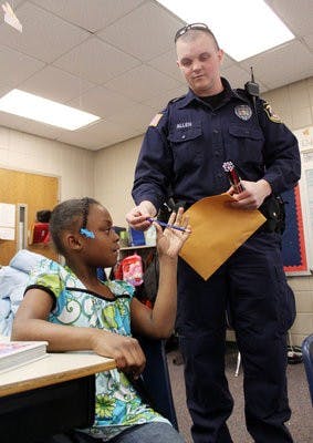 Officer Mitchell Allen gives Diamond Allen, 7, a pencil during his visit to Jeter Primary School Friday morning. (Emily Adams / Photo Editor)