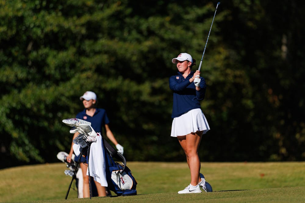 <p>A female golfer in a blue top and white skirt prepares to swing a club, while a second golfer stands nearby with a golf bag. Contributed by Auburn Athletics</p>