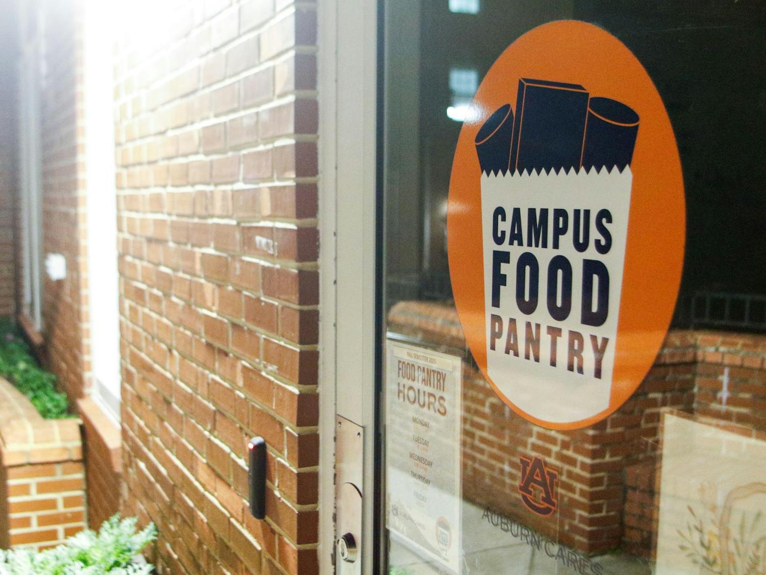 The Auburn Campus Food Pantry's glass door, which features an orange circular sign that reads "CAMPUS FOOD PANTRY," and information about food pantry hours is visible below.