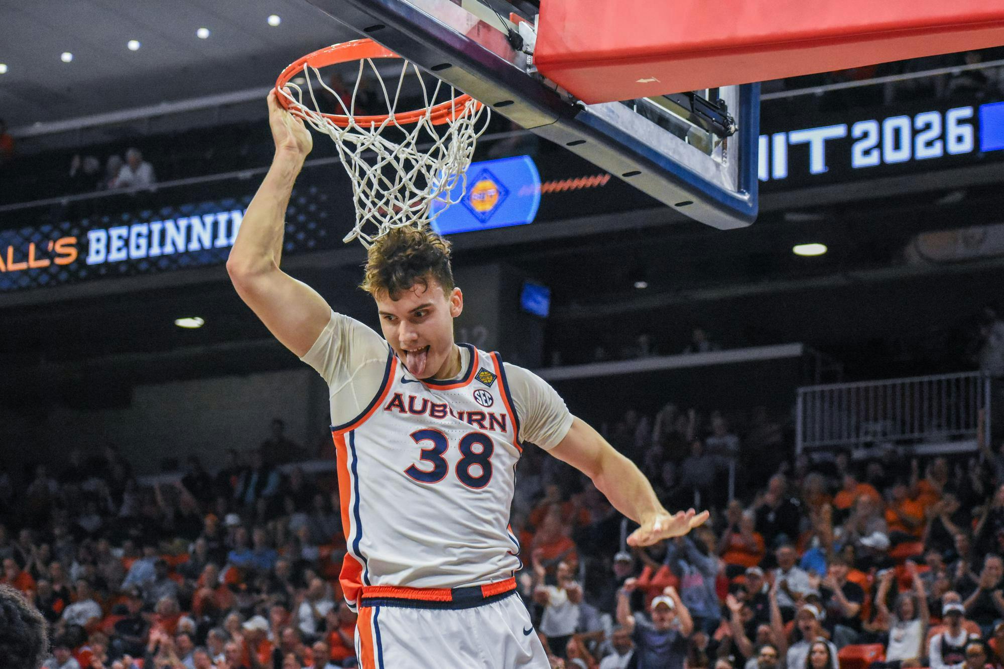 A basketball player in an Auburn uniform hangs from a hoop with excitement, displaying energy and enthusiasm.
