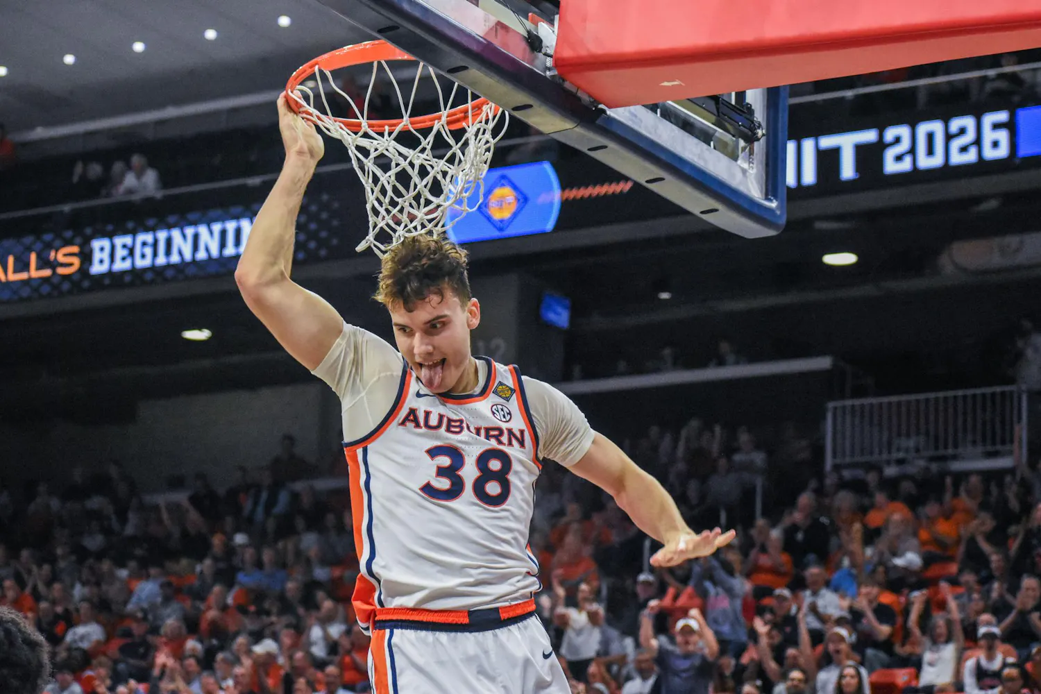 A basketball player in an Auburn uniform hangs from a hoop with excitement, displaying energy and enthusiasm.