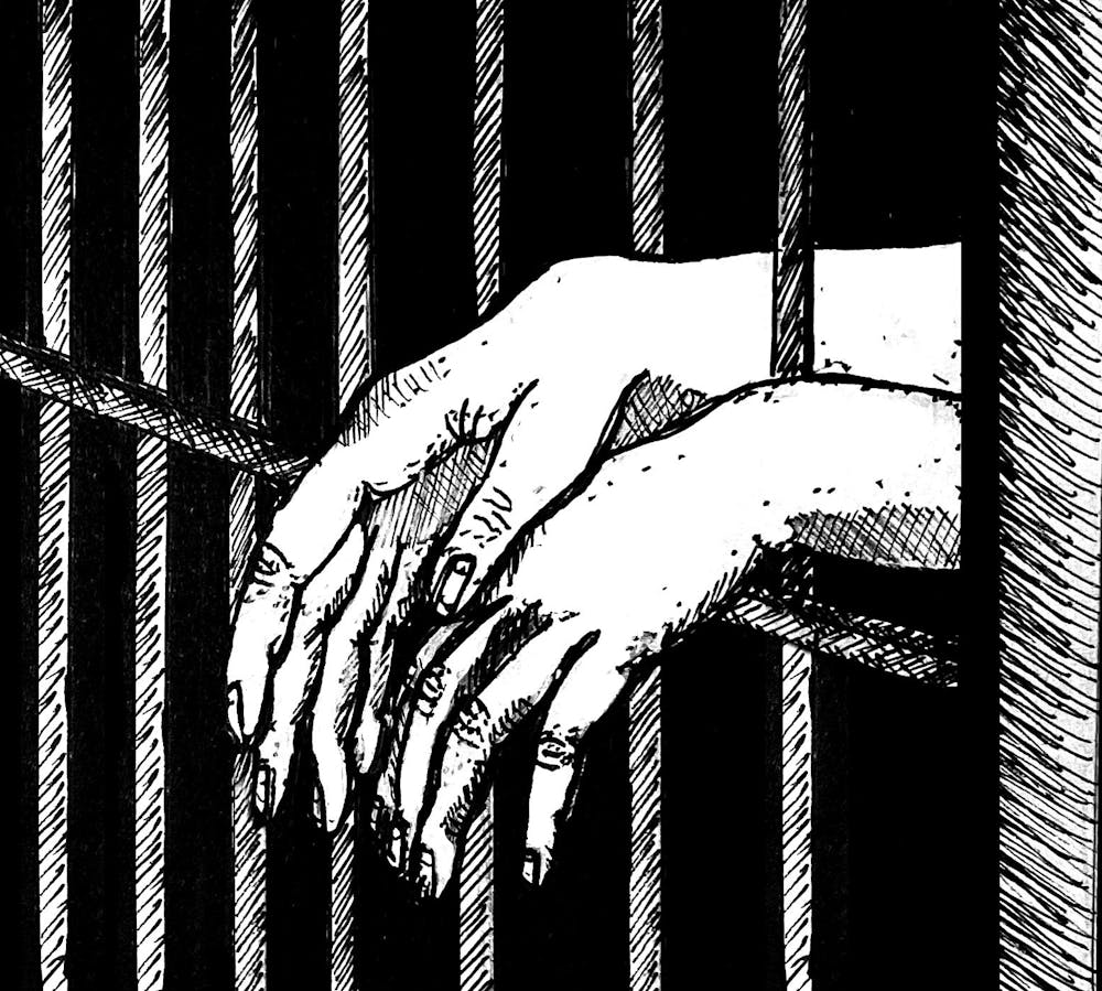 Hands dangling out of the bars of a prison cell. 