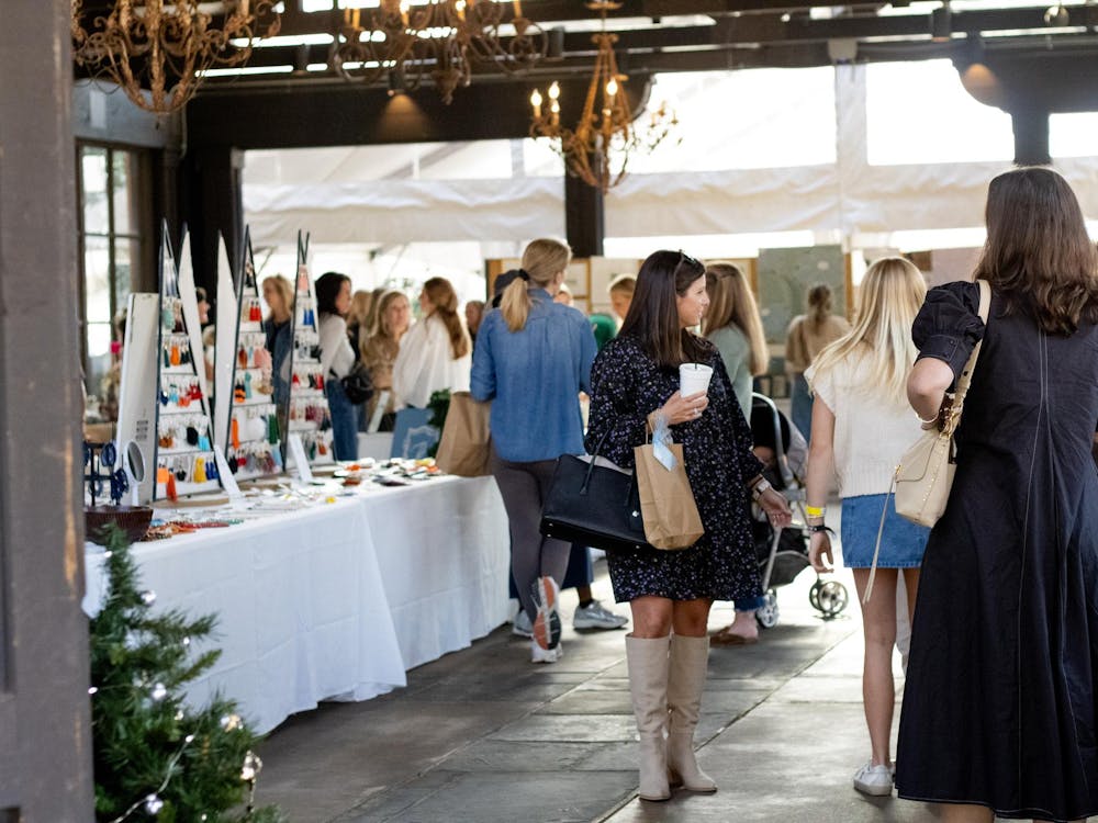 A bustling indoor market features shoppers browsing handmade jewelry displays and vintage goods, with a festive atmosphere highlighted by chandeliers and decorations.